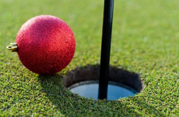 a red christmas bauble next to a golf hole with a flag pole