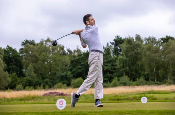 A man wearing a white top and trousers, taking a golf shot.