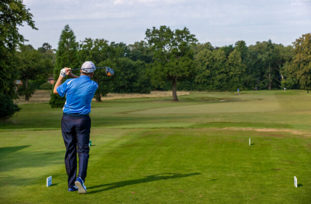 A man wearing a blue top and chinos swinging his golf club.